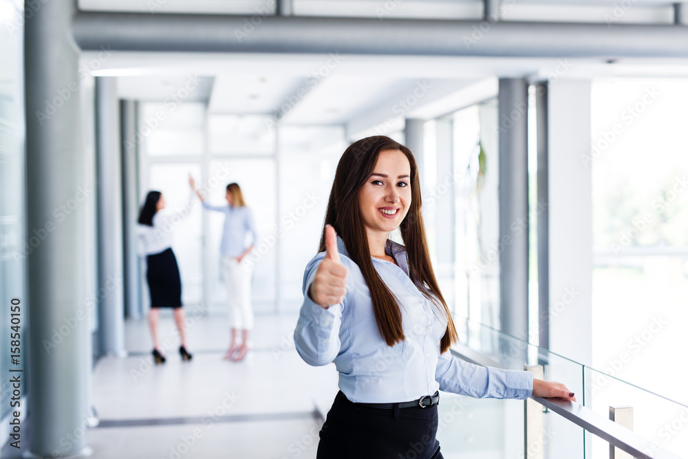 Attractive business woman standing and showing thumbs up while behind are standing her work colleague