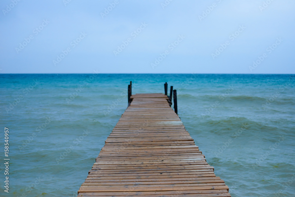 Fototapeta premium Wooden brown pier in waves sea or ocean in sunny day with horizon background and free space for advertising diving product. Perfect place for a fishing in relax time. Water energy on fresh air.