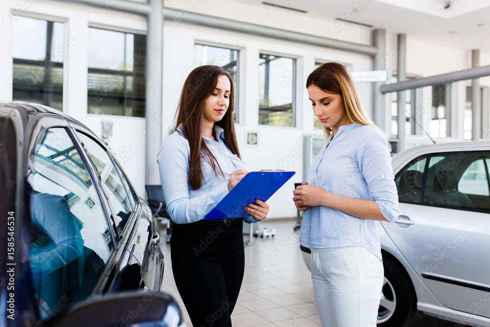 Two women makeing a agreement in modern car dealership