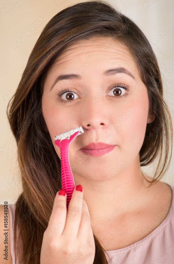 Close up of a beautiful young woman using a shaver pretending to shave her mustache, in a white background Close up of a beautiful young woman using a shaver pretending to shave her mustache, in a white background