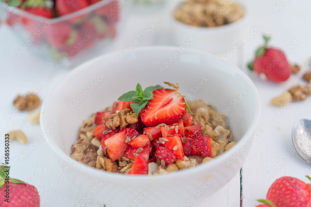Summer healthy breakfast. Oatmeal with strawberries, walnuts, cashew nut, flax seed and mint on a white background on a wooden table. Cleansing the body. Products for weight loss. Wellness. Summer healthy breakfast. Oatmeal with strawberries, walnuts, cashew nut, flax seed and mint on a white background on a wooden table. Cleansing the body. Products for weight loss. Wellness.