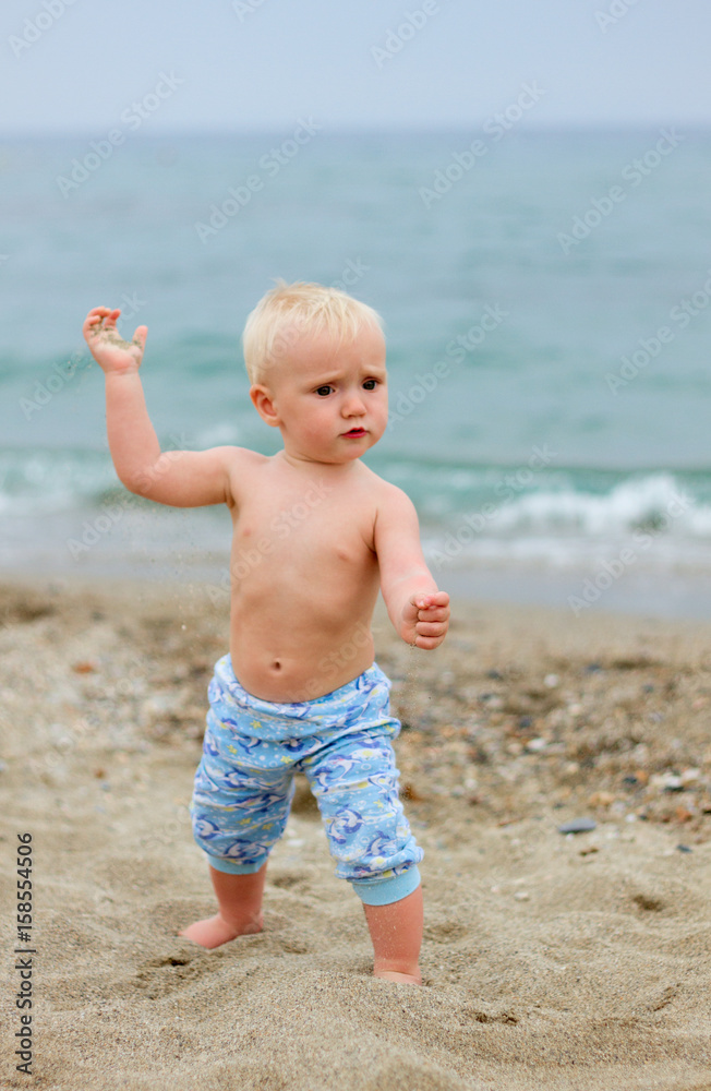 Blond baby standing on the beach on a cloudy day Blond baby standing on the beach on a cloudy day