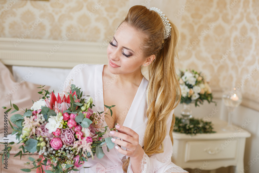 Pretty young girl. Blonde woman with luxurious long hair tail. Boudoir morning of the bride. Taking wedding bouquet in her hands Pretty young girl. Blonde woman with luxurious long hair tail. Boudoir morning of the bride. Taking wedding bouquet in her hands