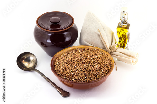 The composition of the Buckwheat groats in a clay pial next to a clay pot and a copper spoon, photo