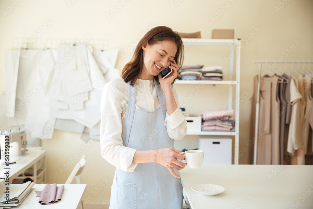 Woman seamstress talking on phone and drinking coffee Woman seamstress talking on phone and drinking coffee