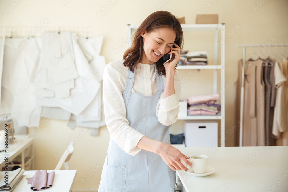 Woman seamstress talking on phone and drinking coffee Woman seamstress talking on phone and drinking coffee