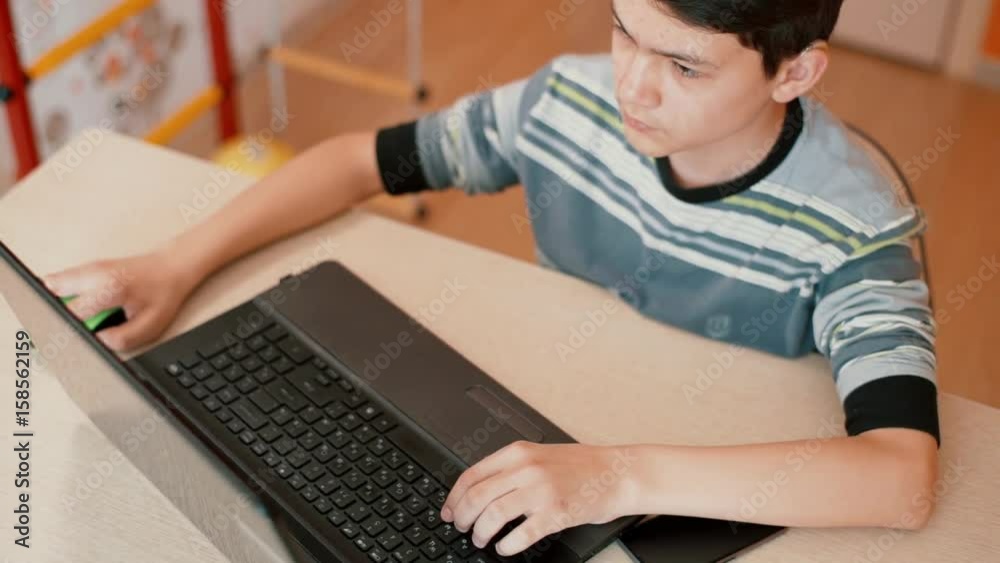 The teenager is sitting at the table using a laptop The teenager is sitting at the table using a laptop
