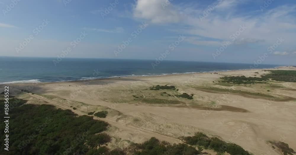 Aerial drone scene of Atlantic Ocean in Pinamar, Miramar, Costa Esmeralda, Buenos Aires Argentina. Camera moving fast backwards. Sand dunes, forest trees and the sea. Blues sky with some clouds. Aerial drone scene of Atlantic Ocean in Pinamar, Miramar, Costa Esmeralda, Buenos Aires Argentina. Camera moving fast backwards. Sand dunes, forest trees and the sea. Blues sky with some clouds.