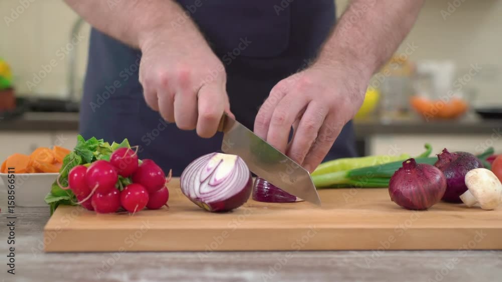 CAUCASIAN CHEF SLICING RED ONION ON A KITCHEN BOARD. DOLLY SHOT, CAMERA SLIDING AROUND TABLE