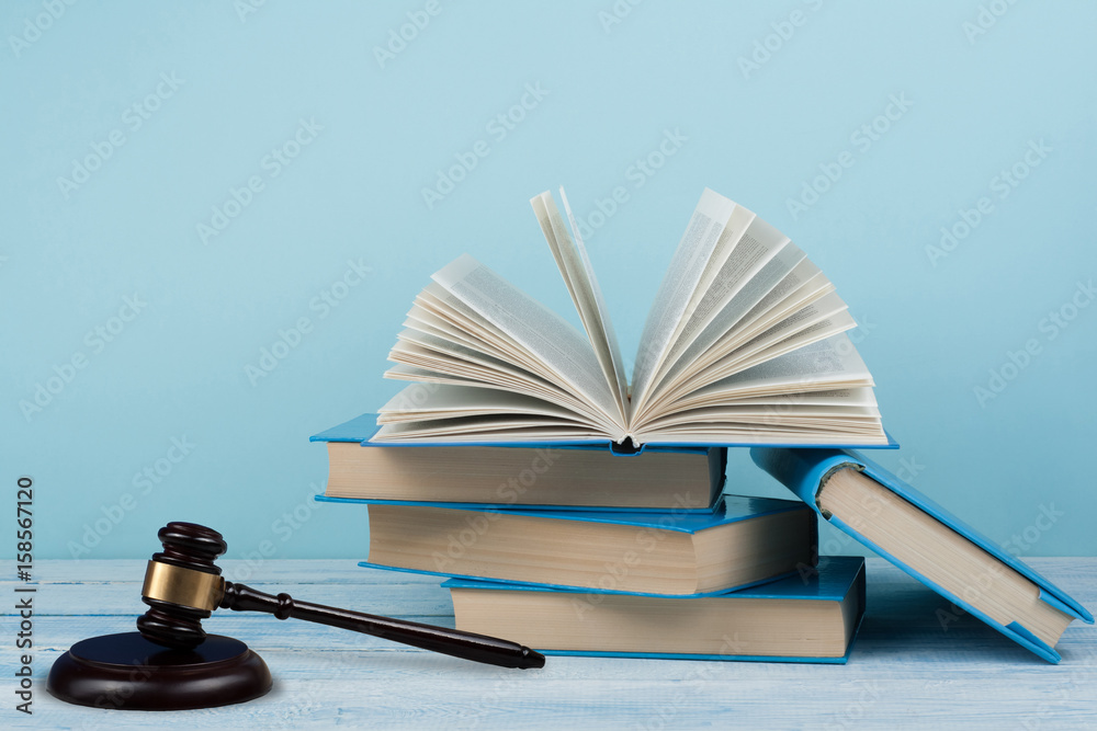 Law concept open book with wooden judges gavel on table in a courtroom or law enforcement office, blue background. Copy space for text. Law concept open book with wooden judges gavel on table in a courtroom or law enforcement office, blue background. Copy space for text.