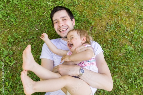 Young father have fun with his little daughter. Man and child are playing in grass.