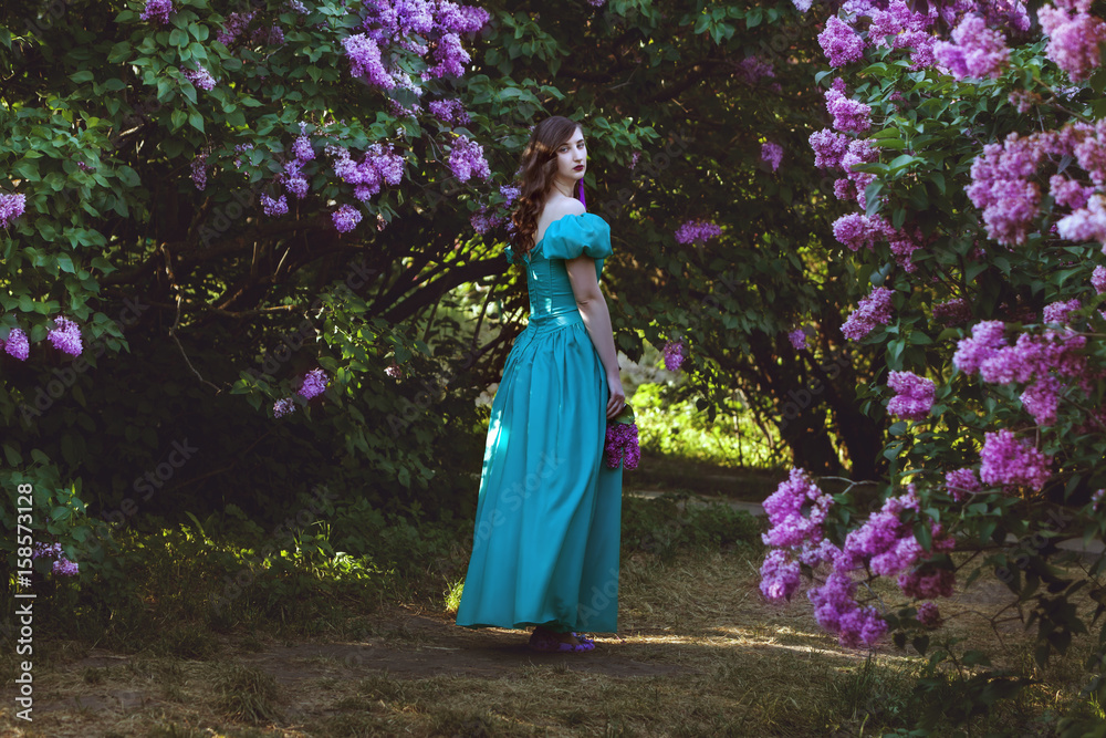 Lovely woman is walking through the garden of a blossoming lilac.