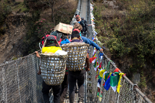 Sherpas carrying a lot of goods in baskets, crossing a bridge on the Everest Base Camp Trek, Sagarmatha National Park, Nepal. 