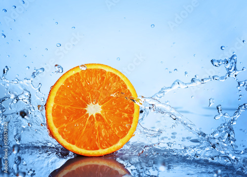 Juicy half an orange in splash of blue water