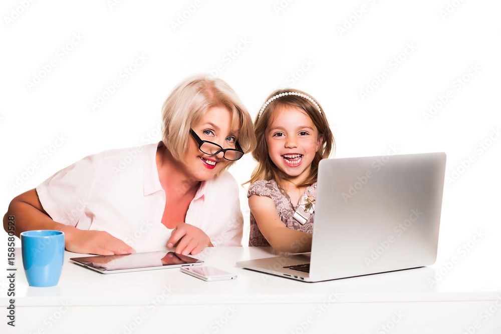 Grandmother and granddaughter uses laptop together and smiling on white background Grandmother and granddaughter uses laptop together and smiling on white background