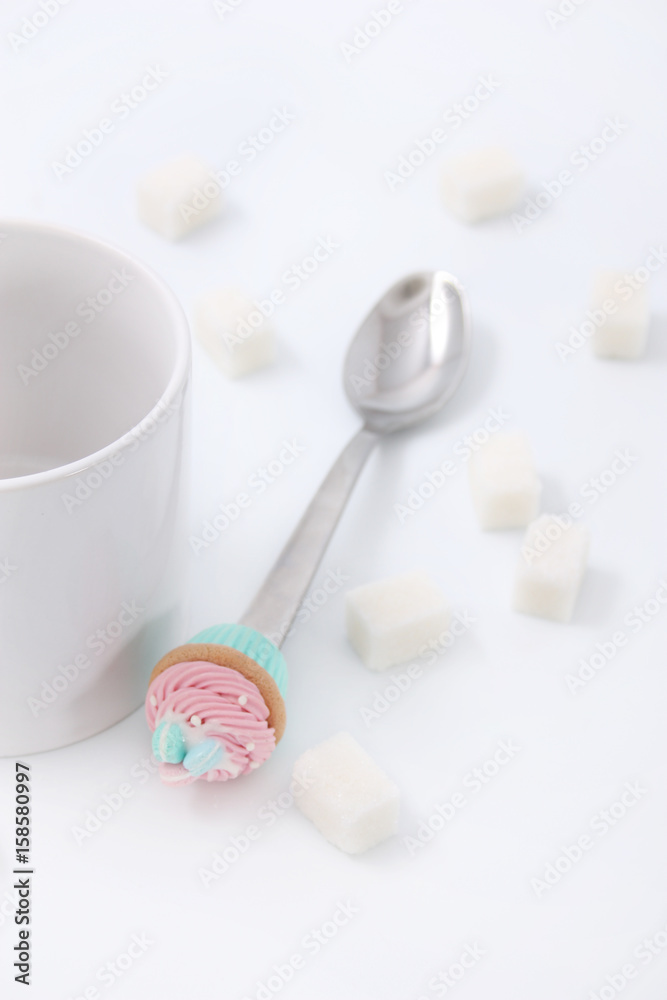 White cup with cubes of sugar and a spoon with a cake on a white background White cup with cubes of sugar and a spoon with a cake on a white background