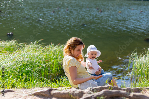 Mother and daughter sitting on the shore of a lake during summer