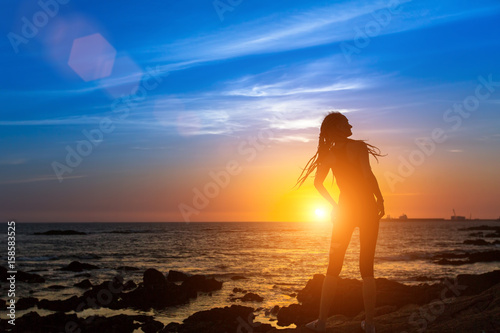 Silhouette of an attractive young woman on the sea shore during a beautiful sunset. © De Visu