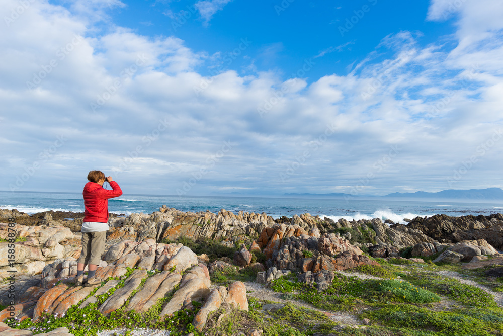 Φωτογραφία Tourist looking with binocular on the rocky coast line at De Kelders, South Africa, famous for whale watching
