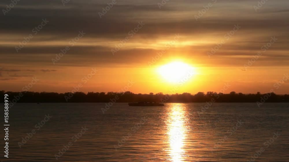 The sunset on the river. A small ship sails on the river against the sunset The sunset on the river. A small ship sails on the river against the sunset