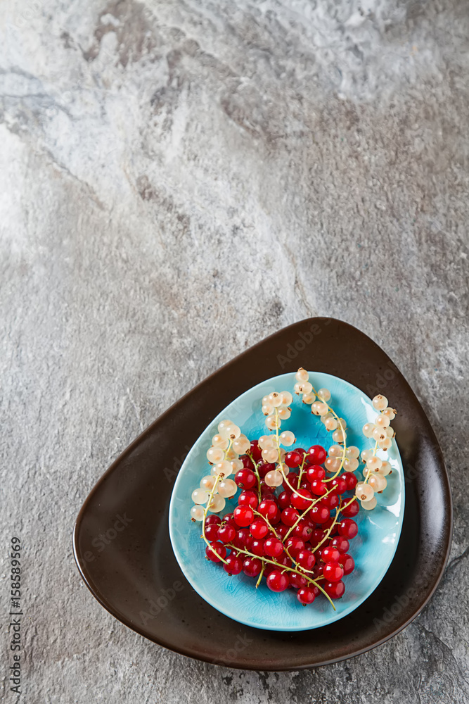 Red and white ripe currant on a blue plate. Dark wood background. Top view