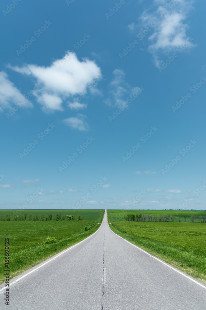 A wide asphalt road between green fields