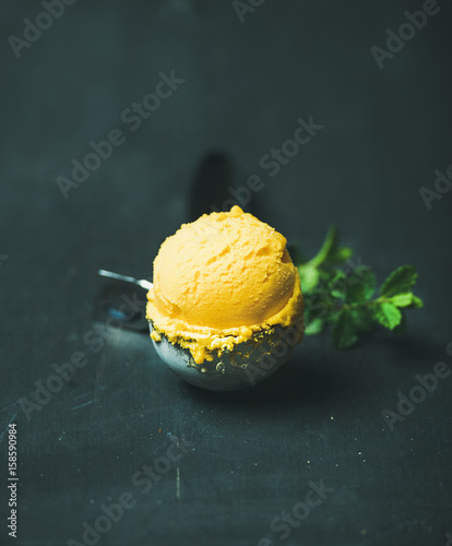 Mango sorbet ice cream scoop in ice cream scooper over black wooden background, close-up. Clean eating, healthy, vegetarian, weight loss, alkaline diet food concept