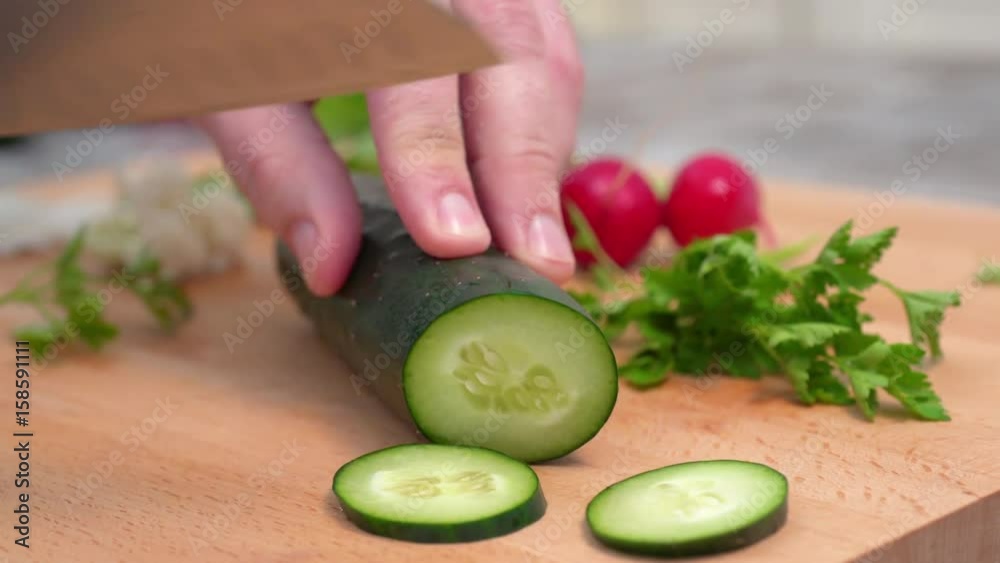 CAUCASIAN HAND SLICING CUCUMBER ON A KITCHEN BOARD. DOLLY SHOT, CAMERA SLIDING FORWARD. CLOSE UP, BLURRED BACKGROUND CAUCASIAN HAND SLICING CUCUMBER ON A KITCHEN BOARD. DOLLY SHOT, CAMERA SLIDING FORWARD. CLOSE UP, BLURRED BACKGROUND