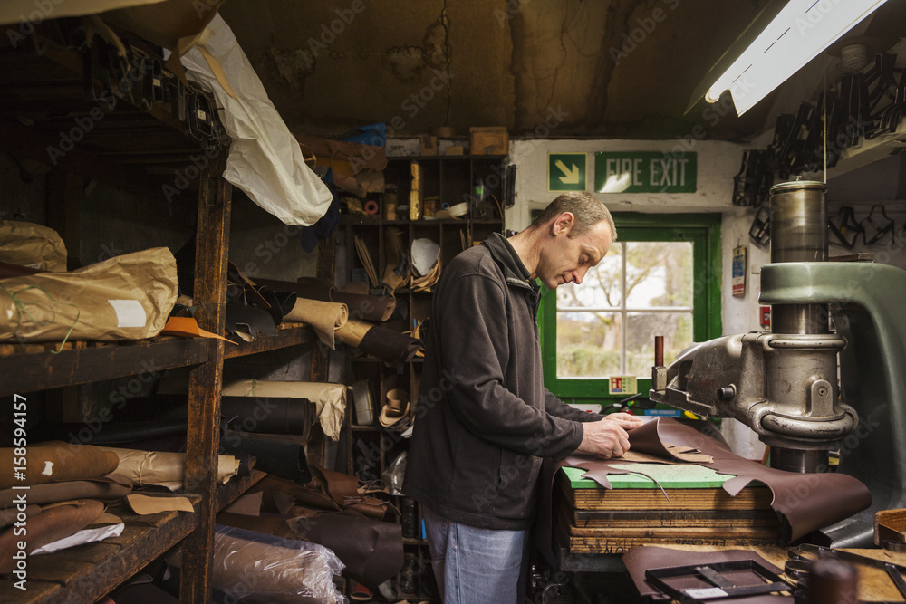 Man standing in a shoemaker's workshop, cutting brown leather. Man standing in a shoemaker's workshop, cutting brown leather.