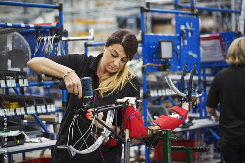 Female skilled factory worker assembling a bicycle in a factory working on the frame and wheels. 