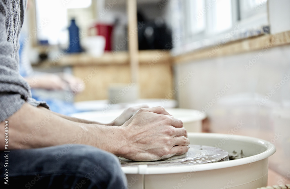 A man using a pottery wheel, with his hands on the clay, throwing pots in a pottery studio. A man using a pottery wheel, with his hands on the clay, throwing pots in a pottery studio.