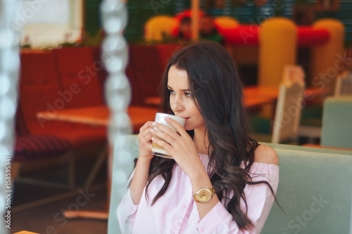 young attractive beauty brunette student girl sitting in outdoor cafe and drink a cup of coffe photo