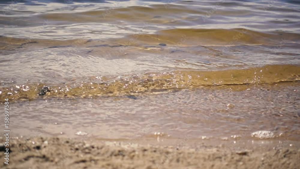 River or lake of transparent waves rolling on a sandy beach. Slow motion