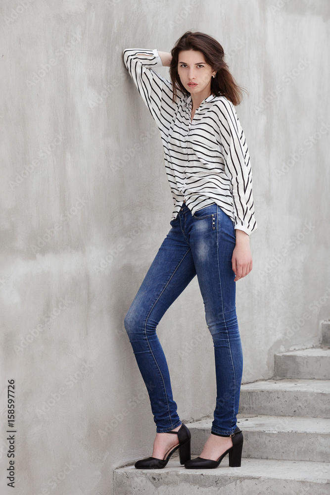 Full length portrait of young fashionable brunette woman practicing model posing outdoors against urban style background of grey concrete wall stairway Full length portrait of young fashionable brunette woman practicing model posing outdoors against urban style background of grey concrete wall stairway