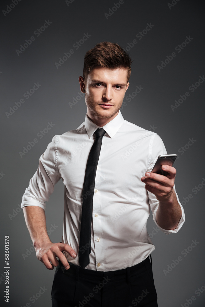 Businessman in formalwear holding mobile phone and looking at camera