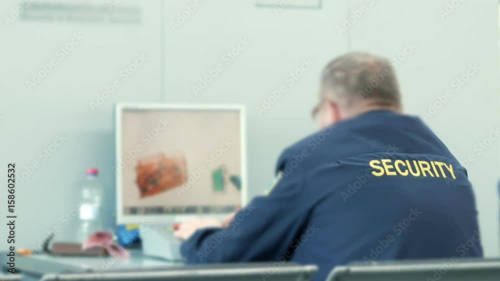 The guard at the airport checks bags on the X-ray. A man looks carefully at the screen of the security system The guard at the airport checks bags on the X-ray. A man looks carefully at the screen of the security system