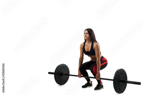 Young athletic woman doing deadlift with a barbell on a white isolated background, standing full squat, legs at shoulder level