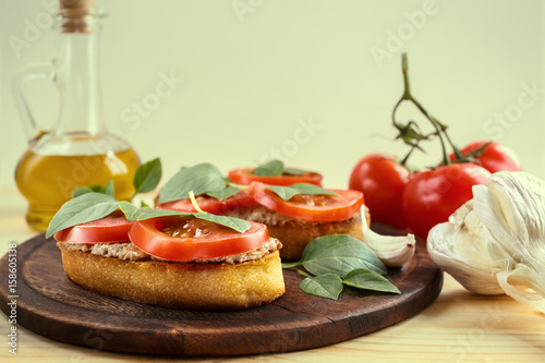 Bruschetta with liver pate, tomatoes and basil on a wooden board. Traditional Italian snack. Close-up. photo