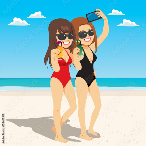 Two young woman friends having fun drinking and taking selfie at beach