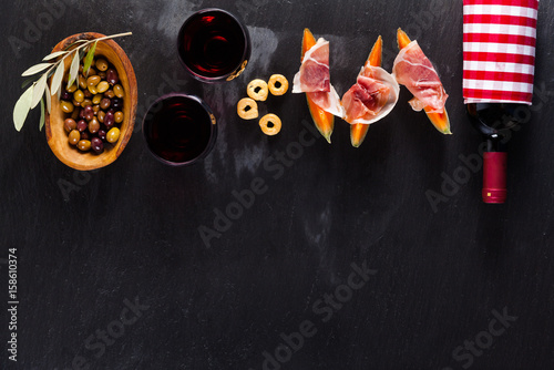 Fototapeta Naklejka Na Ścianę i Meble -  Cold meat cut from different varieties of salami on a dark background with a bottle of red wine and snacks, melons and breadsticks. Italian lunch