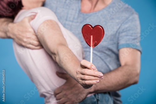 cropped shot of adult couple embracing and holding lollipop in form of heart