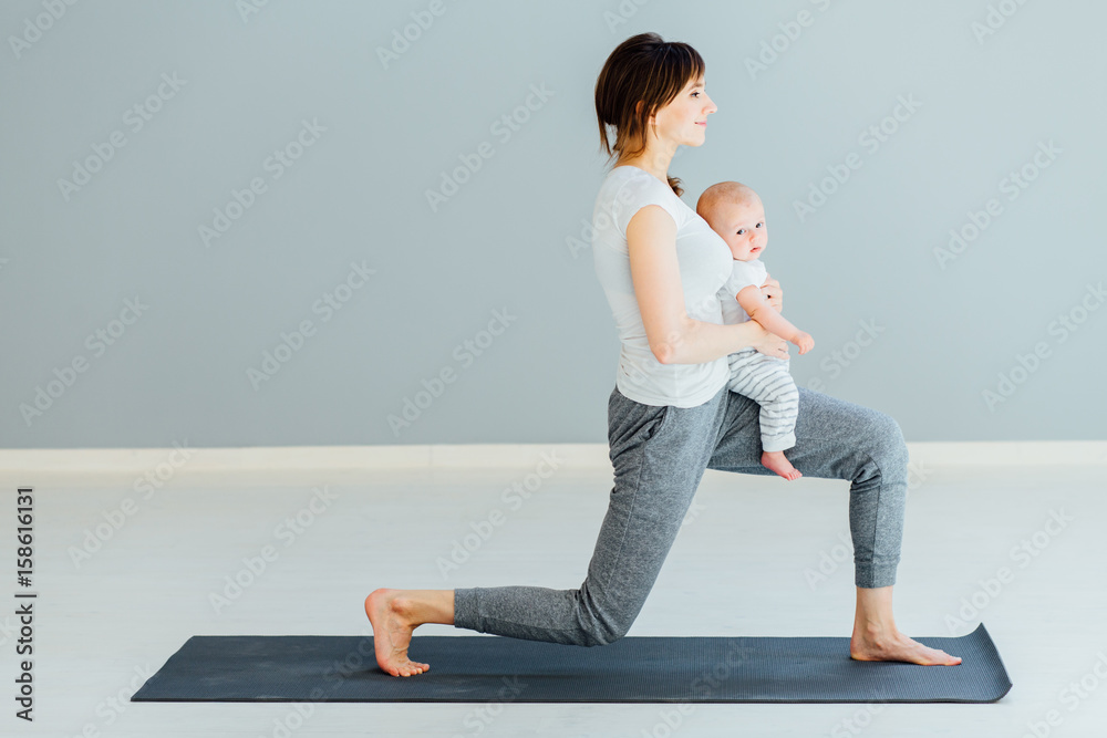 young sporty mother does physical yoga or pilates exercises together with her baby son over gray background. young sporty mother does physical yoga or pilates exercises together with her baby son over gray background.