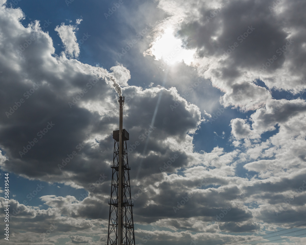 Smoking chimney of oil refinery against cloudy sky and sun Smoking chimney of oil refinery against cloudy sky and sun