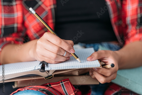Cropped shot of student holding books and writing in notebook with pencil