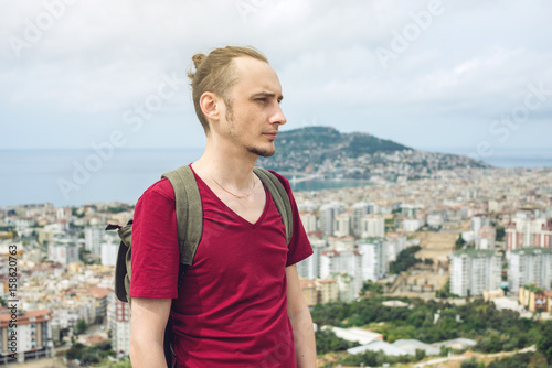 Man traveler with backpack explores the city looking at the panoramic view of the city and the coast. © Artem
