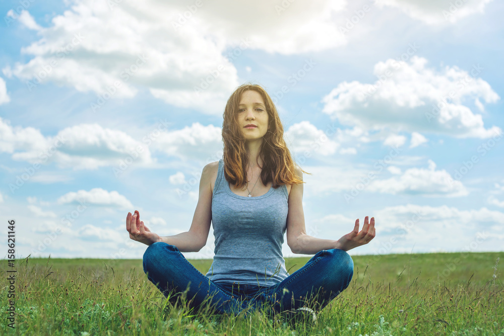 Woman traveler sitting on the meadow with green grass under blue sky with clouds in the Lotus position Woman traveler sitting on the meadow with green grass under blue sky with clouds in the Lotus position