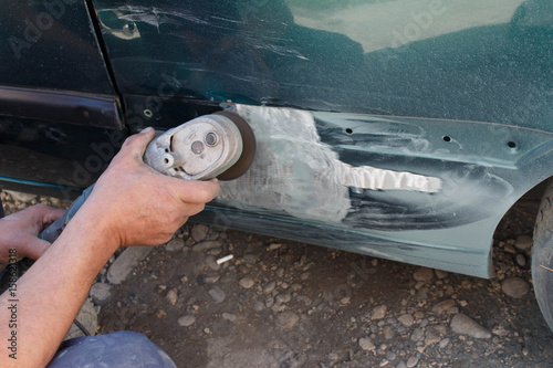 mechanic worker repairman sanding polishing car body and preparing automobile for painting during repair