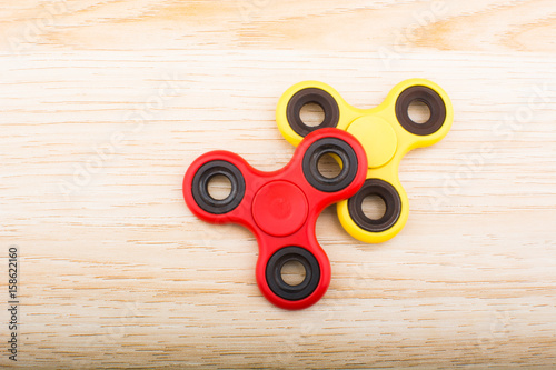 Yellow and red fidget finger spinner stress anxiety relief toy isolated on wooden background.
