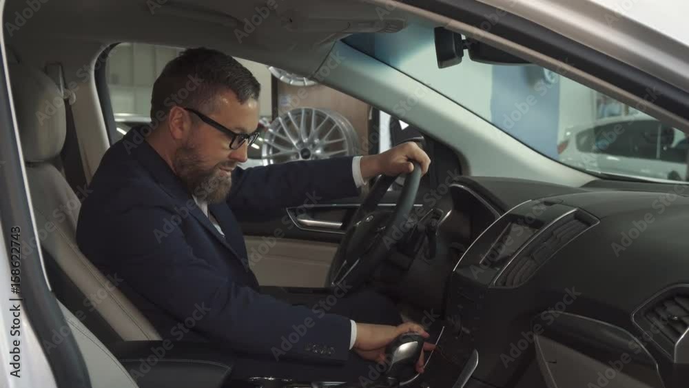 Male bearded customer approving car interior at the dealership. Attractive caucasian man in glasses showing his thumb up inside th vehicle. Handsome brunette guy pushing some buttons on the console Male bearded customer approving car interior at the dealership. Attractive caucasian man in glasses showing his thumb up inside th vehicle. Handsome brunette guy pushing some buttons on the console