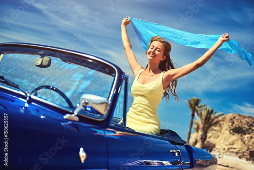 Happy woman with a hands raised sitting in retro car